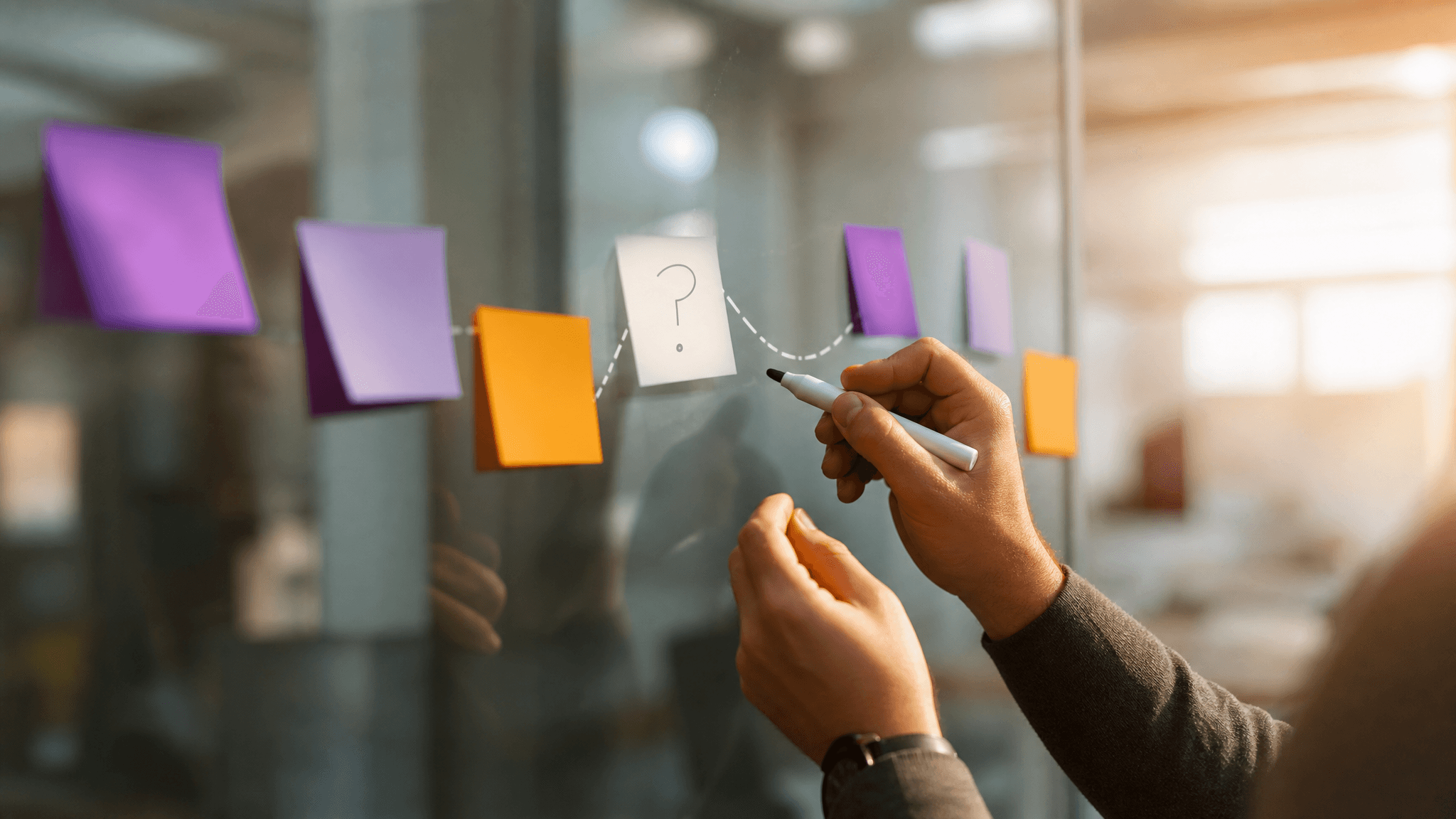 Hands at a glass whiteboard tracing a dotted line between colored sticky notes representing patient touchpoints, one note left blank with a question mark